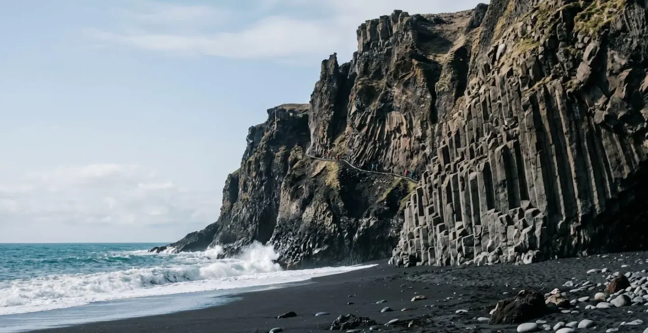 Dramatic volcanic coastal cliffs with visible hiking trail carved into dark basalt rock formations