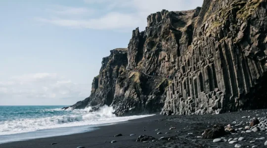 Dramatic volcanic coastal cliffs with visible hiking trail carved into dark basalt rock formations
