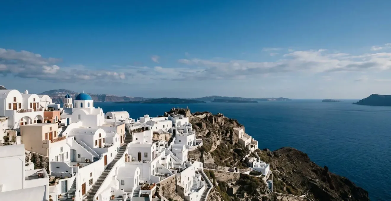 Whitewashed Cycladic village cascading down volcanic cliff overlooking azure Mediterranean waters