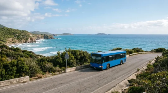 Wide-angle view of a public bus on a winding coastal island road with tropical landscape and ocean in background