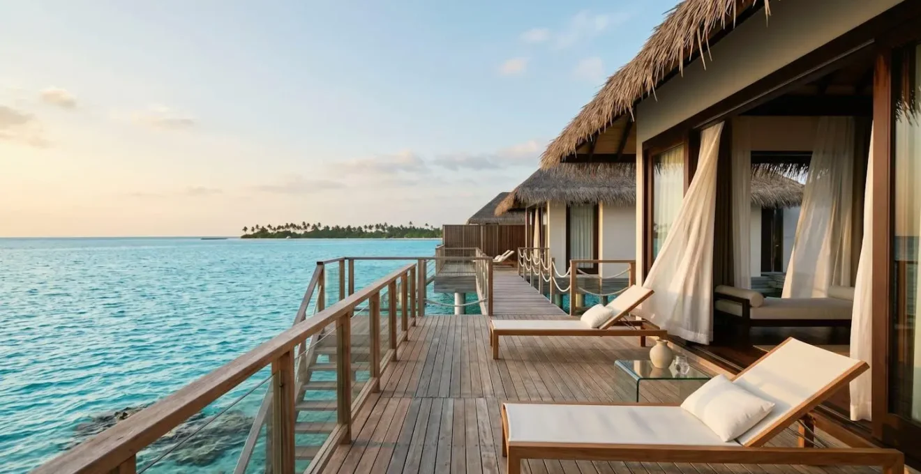 Pristine overwater villa deck suspended above turquoise lagoon with distant tropical island horizon at golden hour