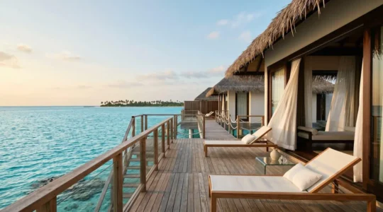 Pristine overwater villa deck suspended above turquoise lagoon with distant tropical island horizon at golden hour