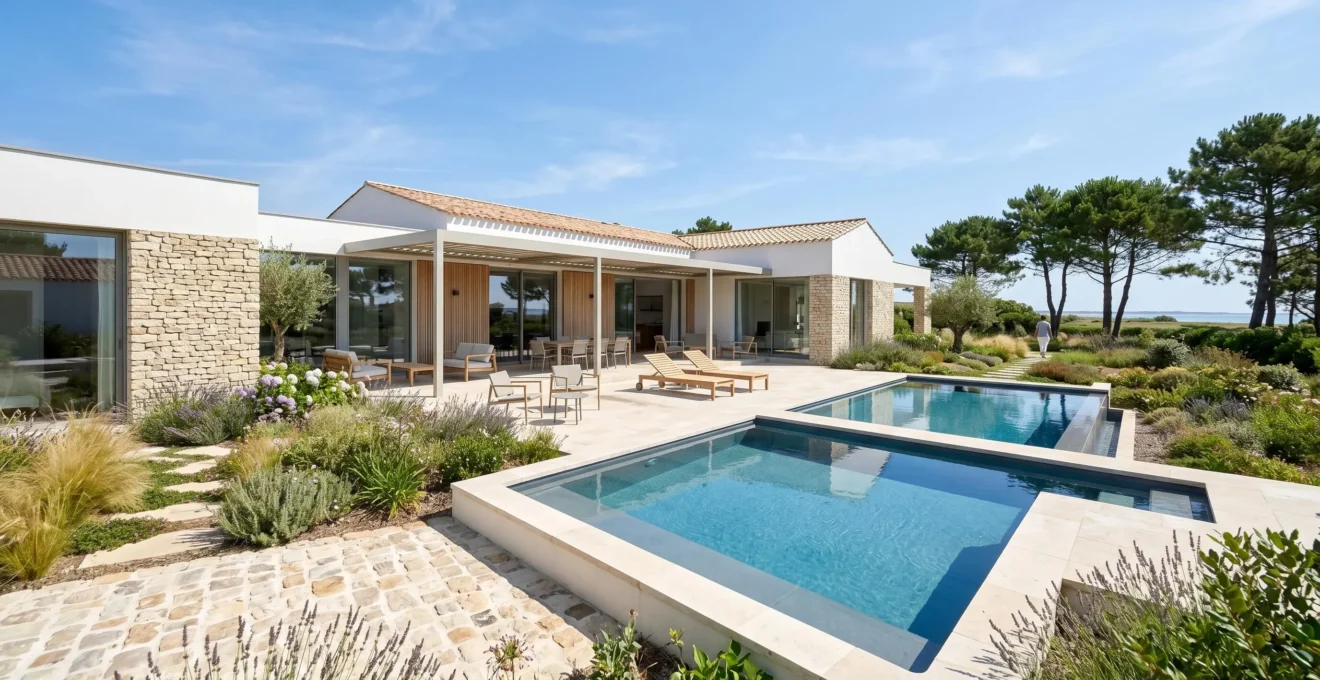 Wide-angle view of private swimming pool surrounded by landscaped garden at contemporary Île de Ré villa, distant figures barely visible, bright summer daylight